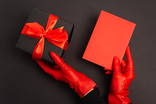 cropped view of person in red gloves holding wrapped gift box and envelope on black