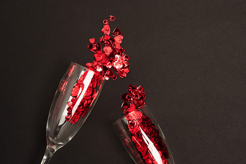 top view of champagne glasses with red confetti hearts on black