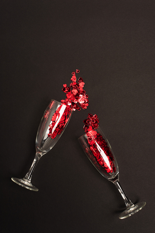 top view of champagne glasses with shiny confetti hearts on black