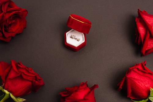 top view of jewelry box with diamond ring near red roses on black
