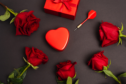 flat lay of metallic heart-shaped box near wrapped present, dark and roses, on black