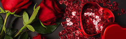 top view of red roses near metallic heart-shaped box and shiny confetti on black, banner