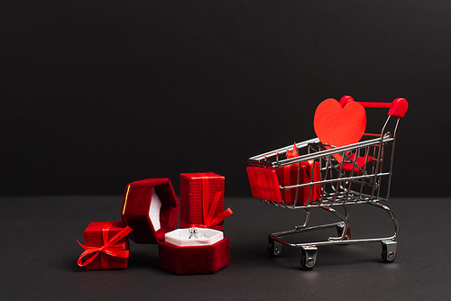 jewelry box with diamond ring near presents and small shopping cart on black