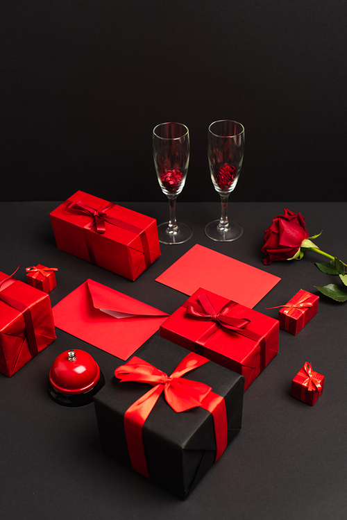 wrapped presents and envelopes near metallic bell, rose and champagne glasses on black