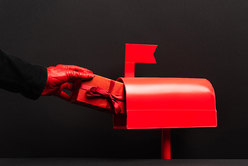 partial view of person in red glove putting present in post box on black