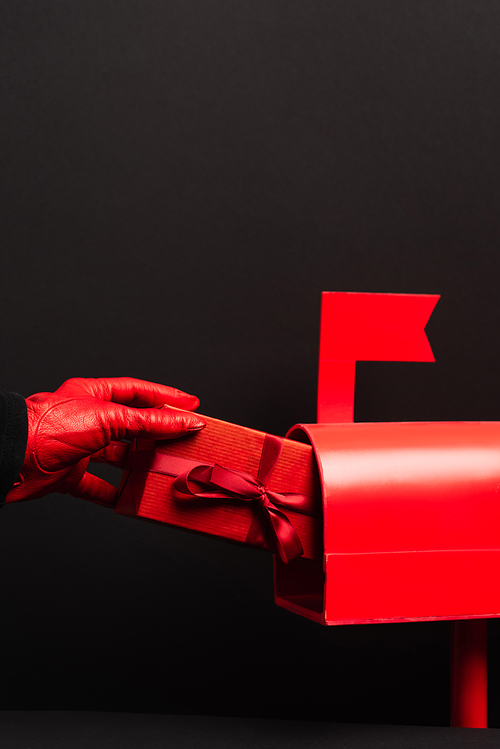 cropped view of person in red glove putting wrapped present in post box isolated on black