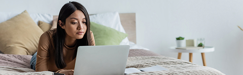 young asian woman working on laptop while lying on bed at home, banner