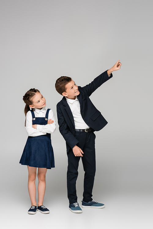 girl in dress standing with crossed arms near boy pointing with finger on grey