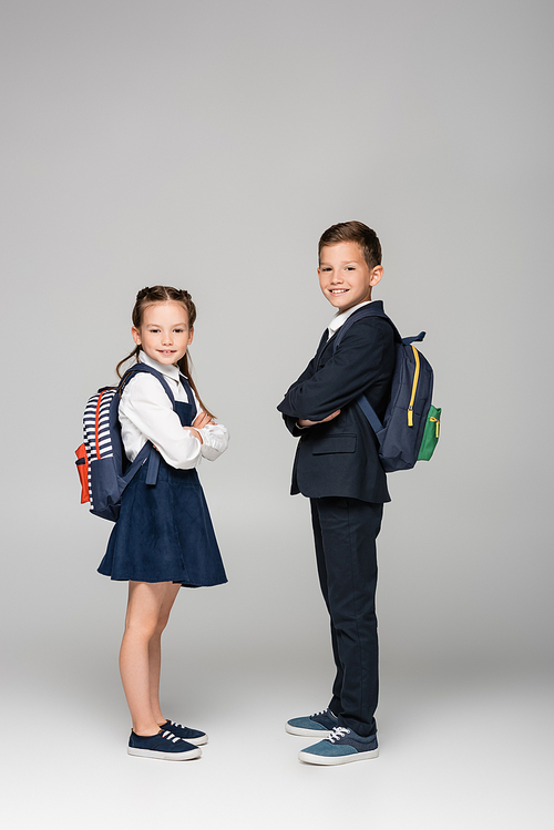 schoolchildren with backpacks posing with crossed arms on grey
