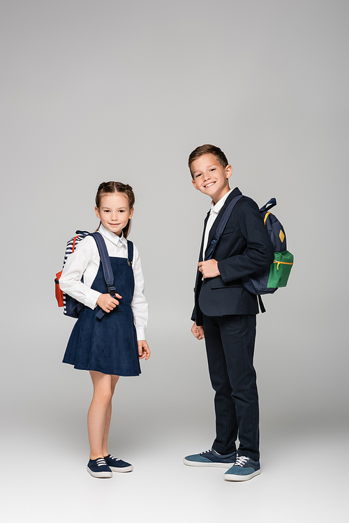 schoolchildren with backpacks standing and smiling on grey