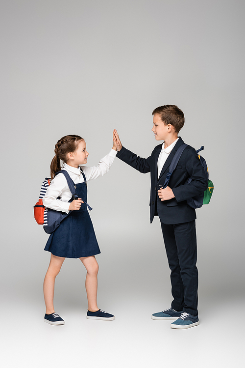 schoolkids with backpacks giving high five on grey