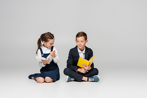 schoolkids sitting with books and smiling on grey