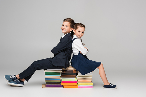 happy schoolkids sitting on pile of books on grey