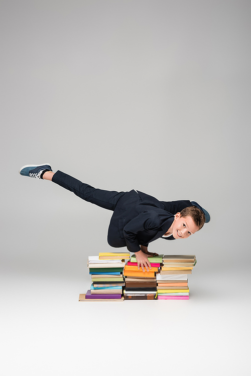 happy schoolboy doing handstand on pile of books on grey