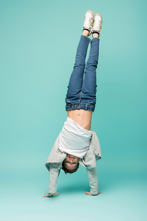 happy boy in denim jeans doing handstand on blue