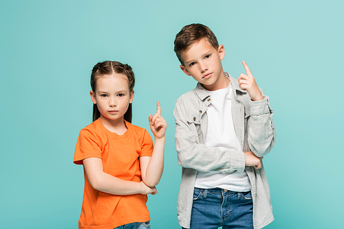 serious kids pointing up with fingers isolated on blue