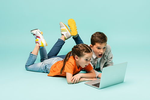 shocked children watching movie on laptop while lying on blue