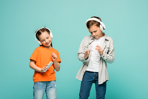 smiling kids in wireless headphones listening music and holding smartphones isolated on blue