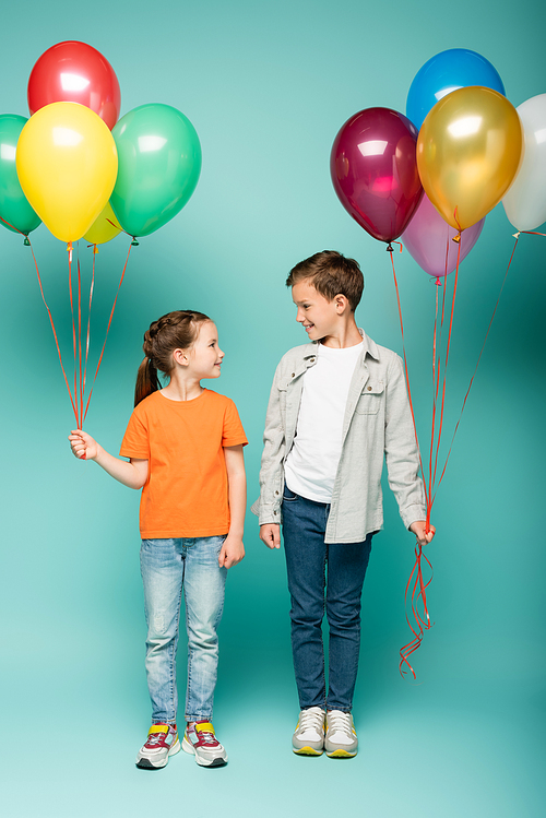 happy children looking at each other while holding colorful balloons on blue