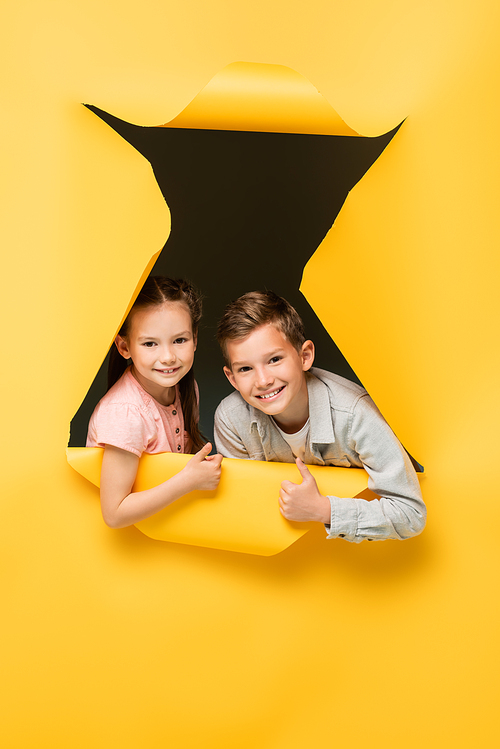 happy kids showing thumbs up and  through hole on yellow background