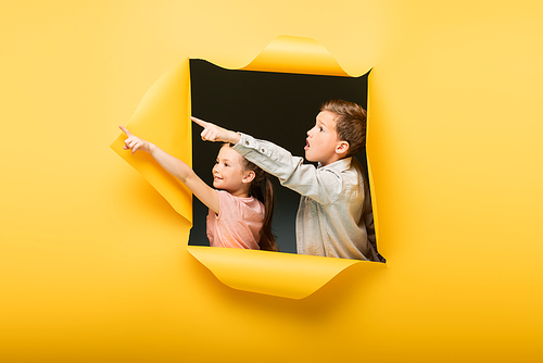 kids pointing away with fingers through hole on yellow background