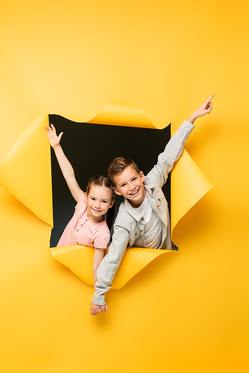 happy children holding hands and smiling through hole on yellow background