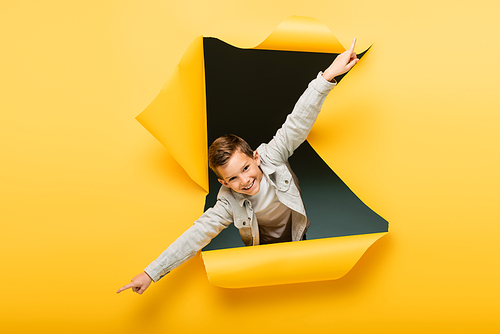 joyful boy with outstretched hands  through ripped hole on yellow background