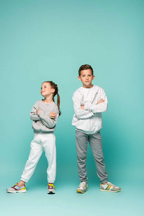 offended boy and girl in sportswear standing with crossed arms on blue