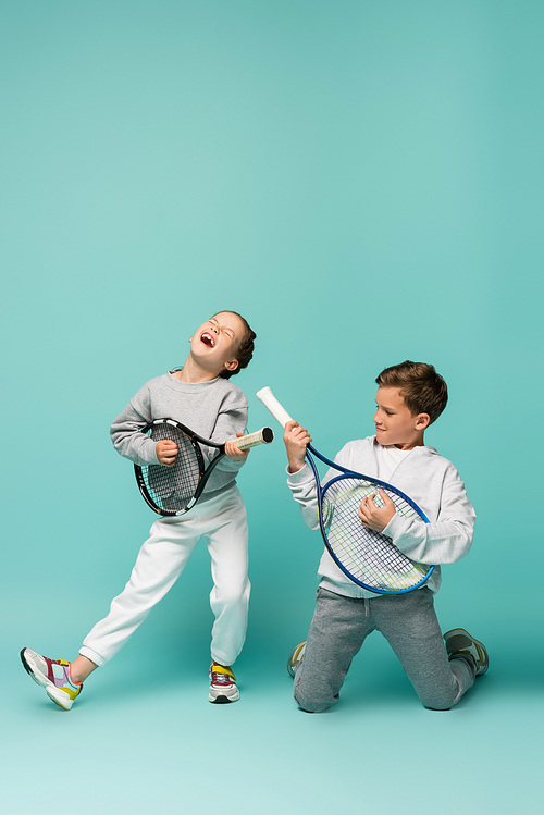 amazed kids holding tennis rackets while singing and pretending performing on blue