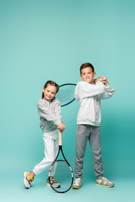 cheerful kids in sportswear standing with tennis rackets on blue