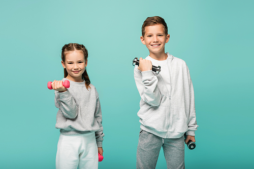 happy kids in sportswear working out with dumbbells isolated on blue