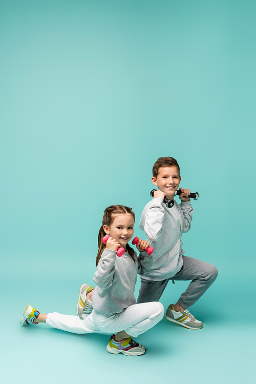 happy kids in sportswear and sneakers working out with dumbbells on blue