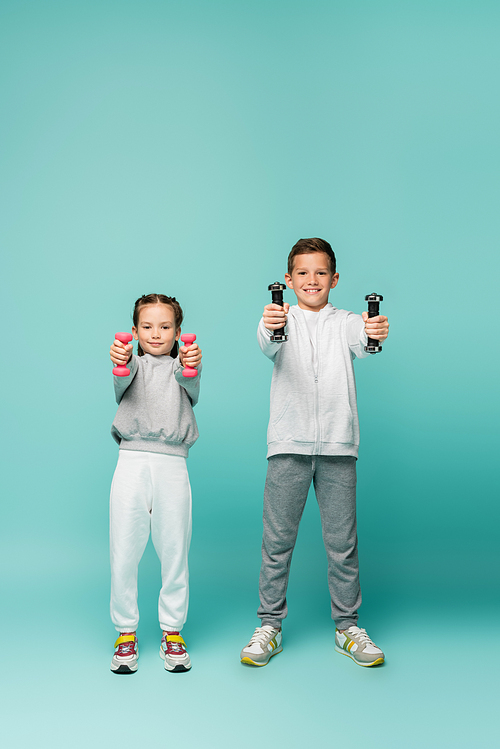 happy children in sportswear and sneakers working out with dumbbells on blue