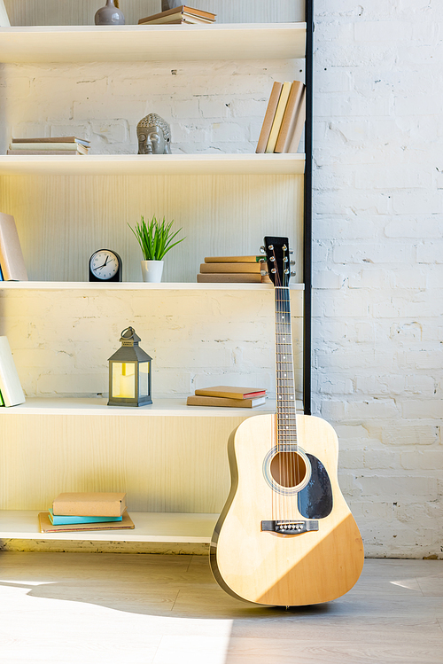 acoustic guitar near shelves with books and clock in sunlight