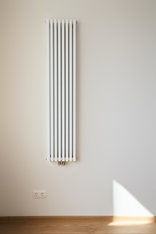 white and modern heating radiator near wall with power sockets