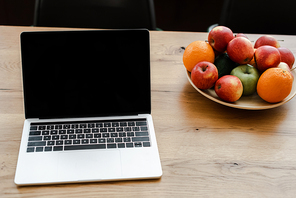 laptop with blank screen standing on wooden table with fruits at home