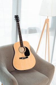 Acoustic guitar on armchair near floor lamp near window in living room