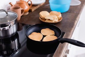 Selective focus of pancakes on frying pan on stove in kitchen