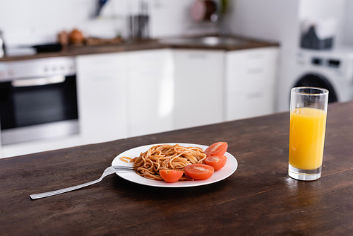 Delicious spaghetti and tomato on plate near glass of orange juice on kitchen table