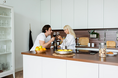 young couple clinking glasses of red wine in kitchen