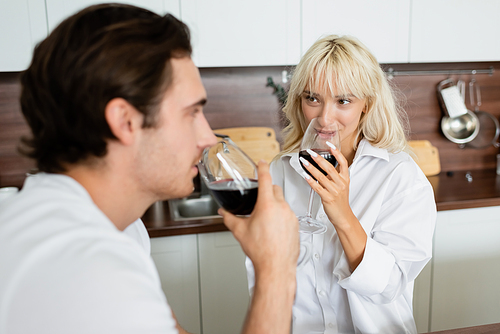 blonde woman drinking red wine and looking at blurred boyfriend