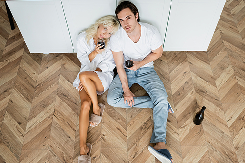 top view of young man and woman holding glasses of red wine while sitting on kitchen floor