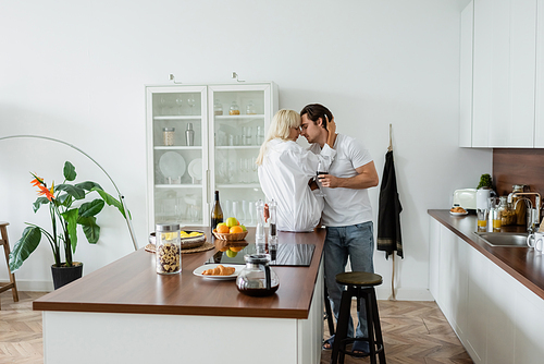 young couple with glasses of wine hugging in modern kitchen