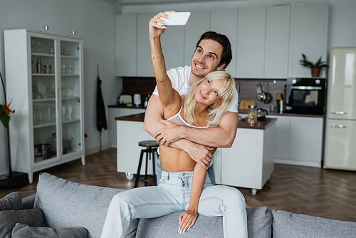 happy woman taking selfie with cheerful boyfriend in living room