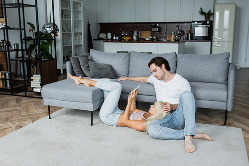 blonde woman using smartphone while lying near boyfriend in living room