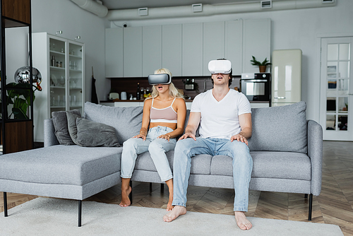 shocked couple in vr headsets sitting on grey couch