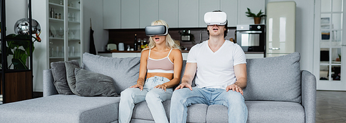 shocked couple in vr headsets sitting on grey couch, banner