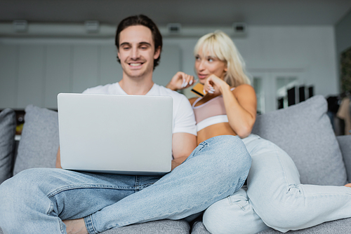 blurred and happy couple with credit card and laptop doing online shopping