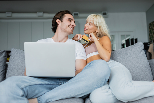 happy couple with credit card and laptop looking at each other doing online shopping