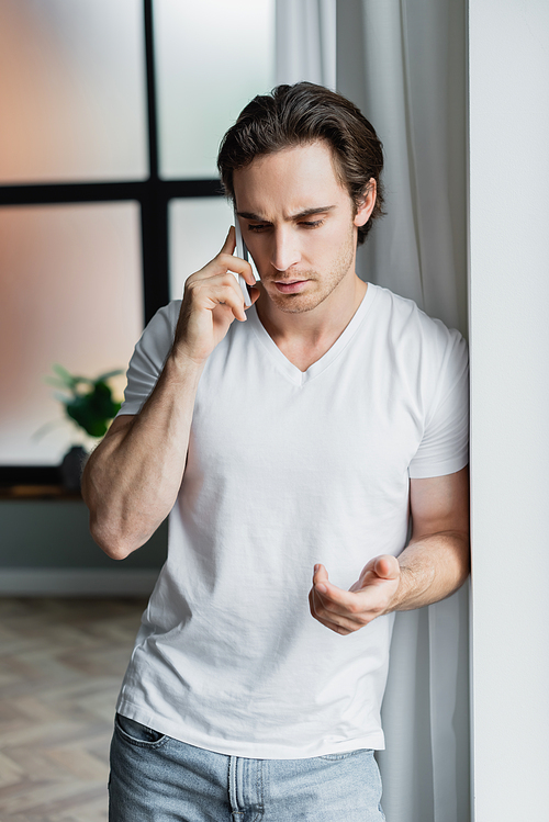young man gesturing while talking on cellphone at home